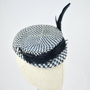 Short brimmed perching cap made in navy and white buntal straw with feathers. 3/4 view