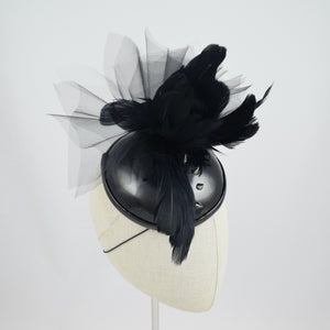 Cocktail hat in wet look vinyl with feathers, tulle, and studs. 3/4 front view.