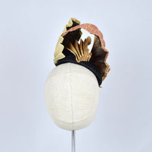 Load image into Gallery viewer, A sculptural fascinator hat with pleated gold fabric on black sinamay, displayed on a cream-colored mannequin head against a light gray background.

