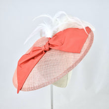 Load image into Gallery viewer, Wide saucer in coral sinamay with coral silk bow and white feathers on a bandeau base. 3/4 front view.
