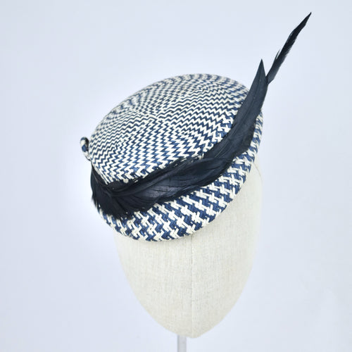 Short brimmed perching cap made in navy and white buntal straw with feathers.  Front view.