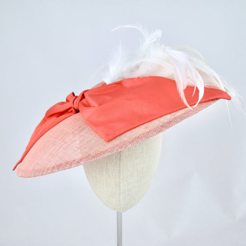 Wide saucer in coral sinamay with coral silk bow and white feathers on a bandeau base. Front view.