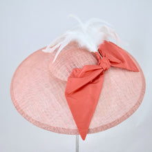 Load image into Gallery viewer, Wide saucer in coral sinamay with coral silk bow and white feathers on a bandeau base. Side view.
