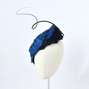 Tear dropped shape percher with peacock blue and black feathers with a dramatic curled quill.  Front view.