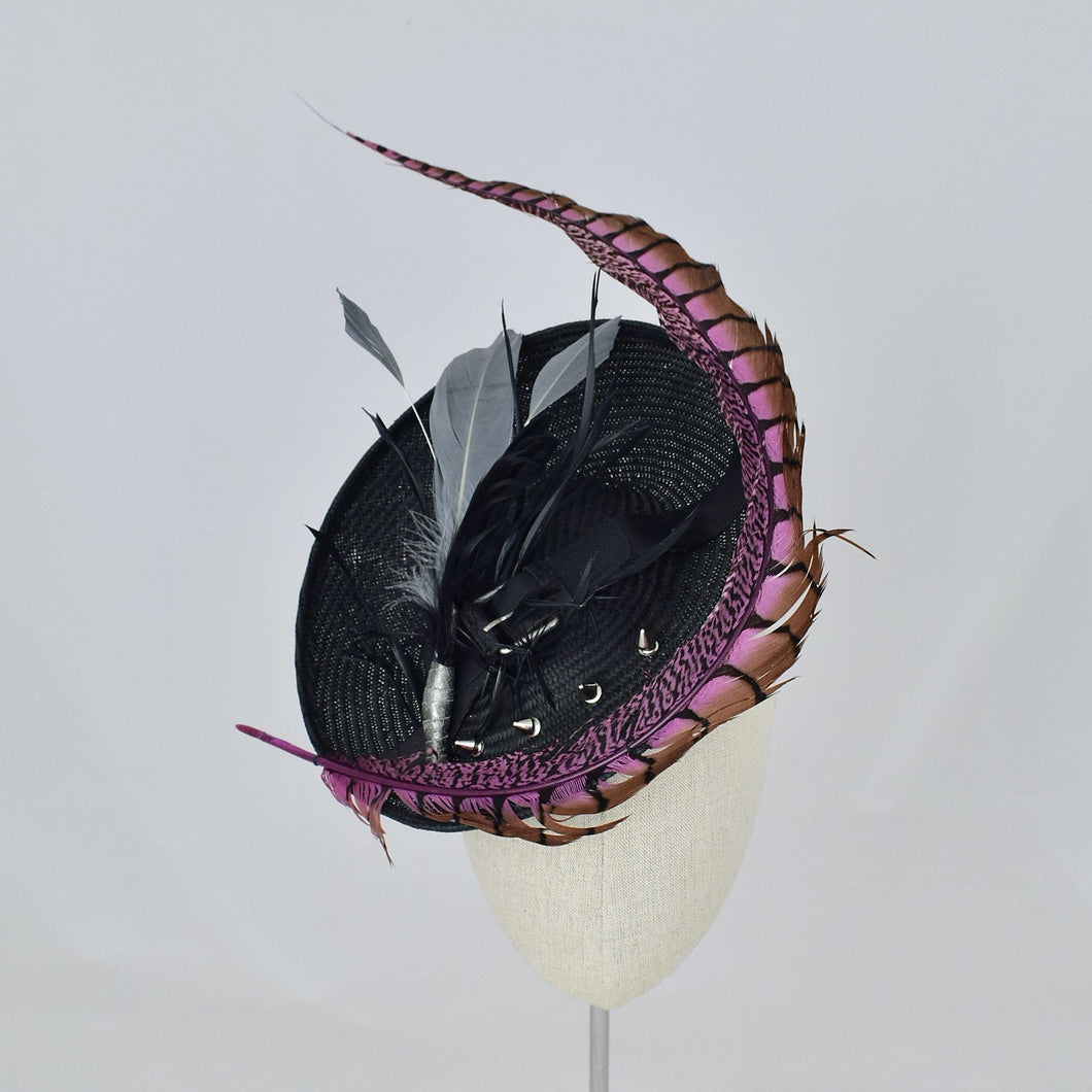 Black parisisal saucer with pink lady amherst feather, black and grey feathers, studs, and a vintage leather buckle. Front view.
