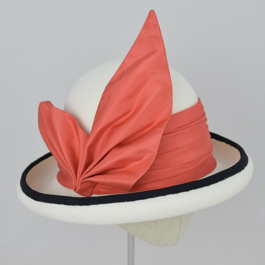 Winter white velour felt bowler with a pleated trim of coral colored silk and black grosgrain ribbon. 3/4 front view.