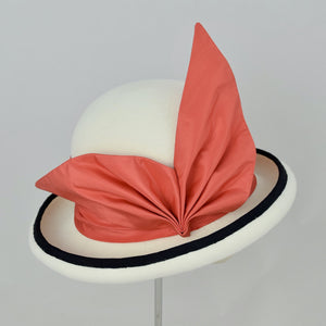 Winter white velour felt bowler with a pleated trim of coral colored silk and black grosgrain ribbon. Side view.