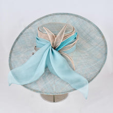 Load image into Gallery viewer, Turquoise and silver sinamay hat with wide, sweeping brim trimmed with turquoise silk chiffon bow and sinamay leaves.  Side view.
