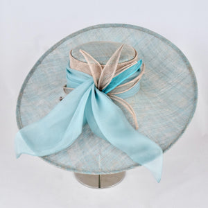 Turquoise and silver sinamay hat with wide, sweeping brim trimmed with turquoise silk chiffon bow and sinamay leaves.  Side view.